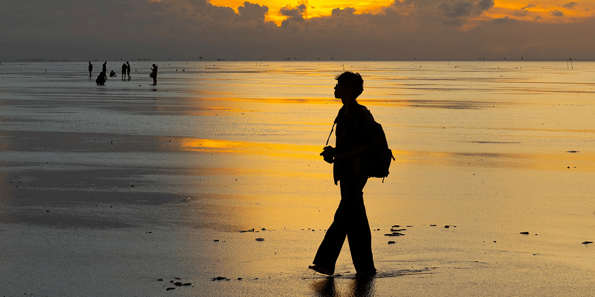 A boy standing on beach with sun kissing the water and the sky touching the water, showing that With Every Pain Comes Ease, With Every Problem Comes a Solution